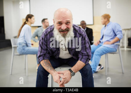 Portrait de bearded man smiling at camera while sitting in chair en face de thérapie de groupe, copy space Banque D'Images