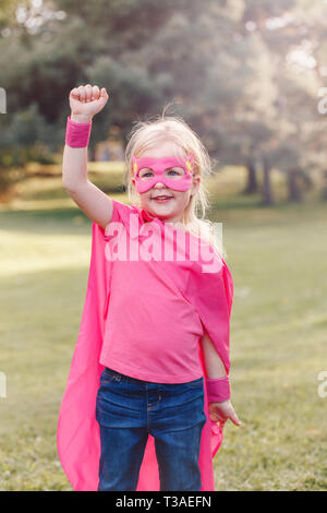 Cute adorable preschool caucasien enfant jouant en costume de super-héros. Enfant fille rose portant masque et cape s'amuser en plein air dans le parc. Happy active ch Banque D'Images