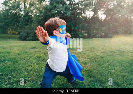 Cute adorable preschool caucasien enfant jouant en costume de super-héros bleu. Kid Boy wearing mask et le cap s'amuser en plein air dans le parc. Happy active chi Banque D'Images