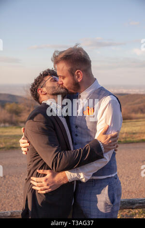 Deux hommes, gay couple hugging chaque d'autres baisers, face à face. intime et comité permanent a proximité, à l'extérieur. Banque D'Images