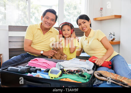 Heureux famille vietnamienne assis sur le lit avec valise ouverte à la location Banque D'Images