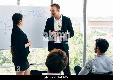 Cheerful Young businessman giving award à employée devant des collègues au cours de séminaire en salle de réunion de bureau moderne Banque D'Images