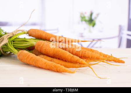Beaucoup de carotte orange bouquet frais entier avec des greens liées par le jute avec fleurs rouge sur blanc en arrière-plan Banque D'Images
