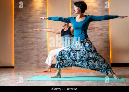 L'homme et la femme brune sont la pratique du yoga en se tenant sur le tapis bleu dans la salle de sport. Banque D'Images