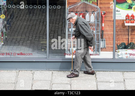 Un vieux monsieur se pencha sur son stick marchant le long d'une chaussée. Banque D'Images