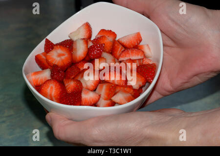 Mûr et sucré rouge et couper les fraises dans une poterie, céramique blanche femme bien entretenu mains tenant un bol poterie céramique blanc avec st fraîchement coupé Banque D'Images