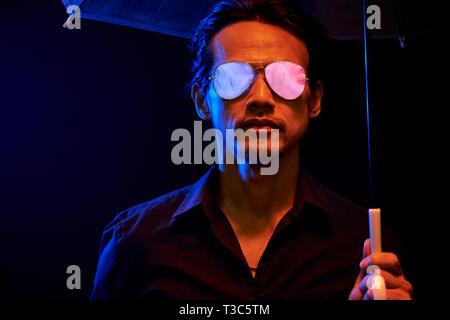 Portrait de l'homme élégant asiatiques portant des lunettes de soleil permanent, sous l'égide contre le fond noir Banque D'Images