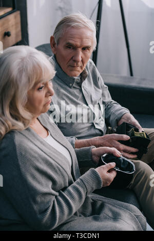 Sad senior couple sitting on couch et holding portefeuille à Accueil Banque D'Images