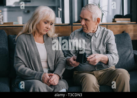 Sad senior couple sitting on couch et holding portefeuille à Accueil Banque D'Images