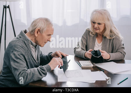 Senior couple holding portefeuille tout en étant assis à table avec les documents Banque D'Images