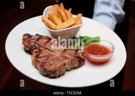 Waiter offering T-bone steak avec frites et hot sauce Banque D'Images