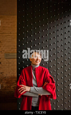 Souriante jeune femme se tient devant une porte en fer clouté. Banque D'Images