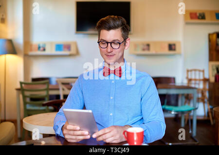 Portrait de jeune homme portant des vêtements de cause alors qu'il était assis au bureau et à l'aide de sa tablette numérique. Les petites entreprises. Banque D'Images