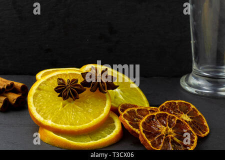 Ingrédients naturels pour faire des fruits parfumés thé : tranches d'orange, l'anis étoilé, les rondelles d'agrumes, d'épices. Verre transparent en verre sur une sombre backgroun Banque D'Images