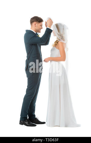 Happy groom lifting Bridal Veil et à la recherche de brides face isolated on white Banque D'Images