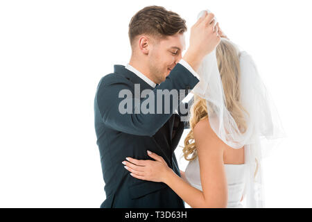 Happy groom lifting Bridal Veil et à la recherche de brides face isolated on white Banque D'Images