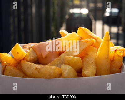 Fort de frites avec sauce. Gros plan sur une boîte de frites avec sauce. La lumière du jour, l'arrière-plan flou derrière. Concept de restauration rapide et les aliments malsains. Banque D'Images