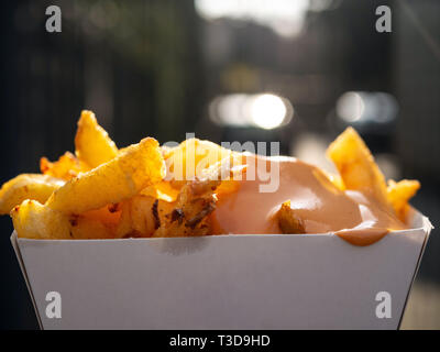 Fort de frites avec sauce. Gros plan sur une boîte de frites avec sauce. La lumière du jour, l'arrière-plan flou derrière. Concept de restauration rapide et les aliments malsains. Banque D'Images