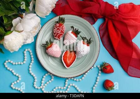 Fraises enrobées de chocolat blanc et rose se situent sur une plaque sur fond bleu turquoise Banque D'Images