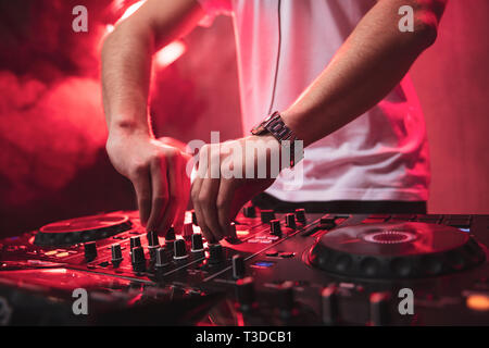 Mixage Dj sur party festival avec la lumière rouge et de la fumée en arrière-plan - la vie nocturne d'été voir de disco club à l'intérieur. Se concentrer sur les mains Banque D'Images