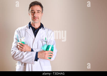 Dentiste en robe blanche avec des produits et outils en mains et mains croisées avec poche. Composition horizontale. Vue de face. Banque D'Images