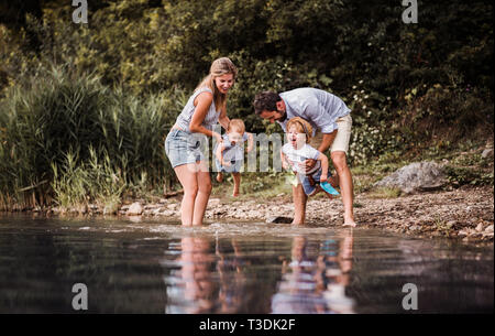 Une jeune famille avec deux enfants tout-petits à l'extérieur de la rivière en été. Banque D'Images