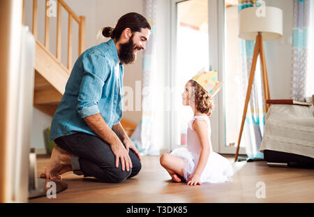Vue de côté de petite fille avec une princesse couronne et jeune père de famille à la maison, à jouer. Banque D'Images