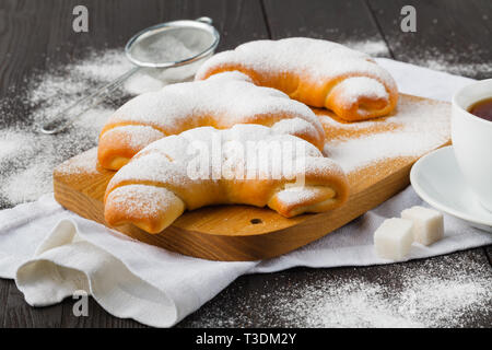 Rouleaux de biscuits remplis de confiture avec du sucre en poudre sur le dessus sur plaque sur table en bois Banque D'Images