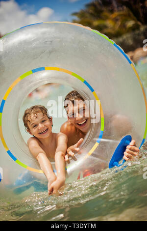 Portrait de jeune garçon et son père jouant avec un tube intérieur dans la mer lors d'une plage. Banque D'Images