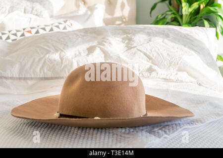 La femme sun hat beige avec garniture et large bord sur un lit moelleux, avec la lumière du soleil qui brille à l'intérieur. Représentant des fêtes, détente et de sortir de la mode. Banque D'Images