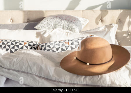 La femme sun hat beige avec garniture et large bord sur un lit moelleux, avec la lumière du soleil qui brille à l'intérieur. Représentant des fêtes, détente et de sortir de la mode. Banque D'Images