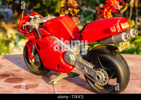Une moto jouet rouge gros plan isolé avec des couleurs chaudes. photo a pris à partir d'un jardin. Banque D'Images
