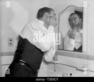 En homme modeste appartement bains regarde dans le miroir comme il se rase lui-même ca. 1938 Banque D'Images