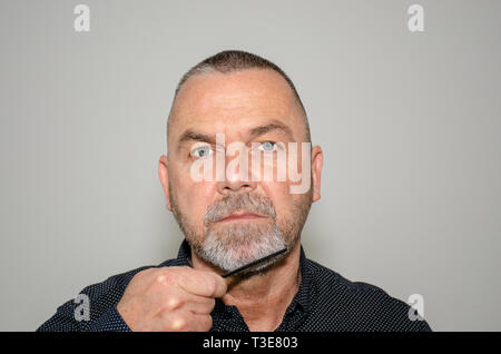 Homme d'âge moyen barbu peignant sa barbiche grisonnante barbe en regardant la caméra dans un concept d'hygiène et de soins personnels Banque D'Images