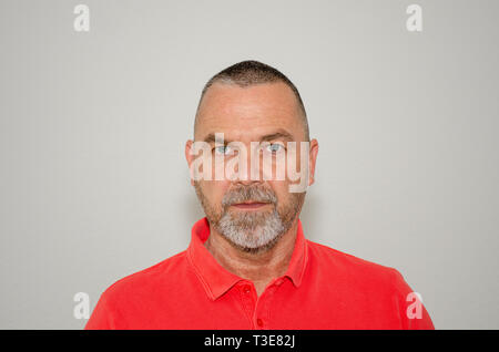 Un homme d'âge moyen avec une énigmatique expression impassible regardant fixement la caméra dans un gros plan de la tête et des épaules sur un arrière-plan gris studio Banque D'Images