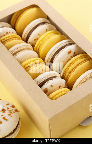 Macarons colorés avec différents matériaux dans une boîte-cadeau sur fond jaune. Banque D'Images