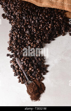 Portrait d'un sac de toile de grains de café torréfiés sur la surface avec une cuillerée de café à la fin du déversement. Banque D'Images