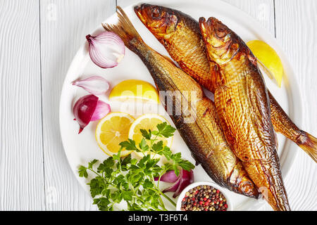 Ensemble de harengs fumés à chaud avec les tranches de citron, le persil et l'oignon rouge sur une assiette blanche sur une table en bois, vue horizontale à partir de ci-dessus, close-up Banque D'Images