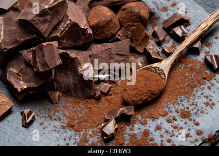 Chocolat bio noir ou au lait et de poudre de cacao pièces sombre sur fond de béton Banque D'Images