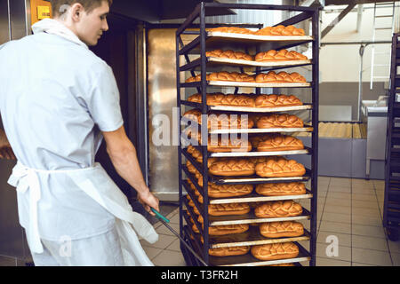 Le Baker pousse un plateau avec du pain dans la manufacture de boulangerie. Banque D'Images