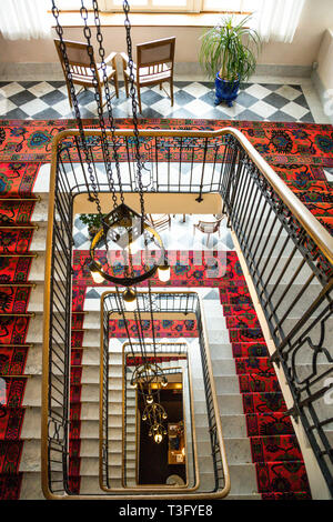 La cage d'escalier de l'hôtel Waldhaus à Sils im Engadin/Segl, en Suisse, vue de dessus, descend sur plusieurs étages : des tapis d'escalier à motifs rouges, des rampes en fer forgé et des lustres suspendus par des chaînes mènent à la salle en marbre à damier du rez-de-chaussée. Le grand hôtel est géré en entreprise familiale depuis 1908. Banque D'Images