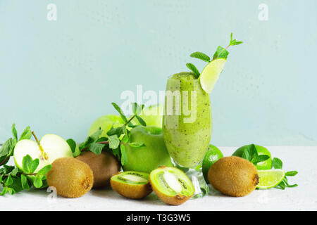 Un verre de smoothie aux fruits vert sur la table, boire et ingrédients pour elle, fond bleu Banque D'Images