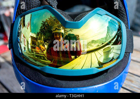 Réflexions de femme et d'enfants et de belles montagnes sur un masque de ski, verre de vin, du café et des gâteaux Banque D'Images