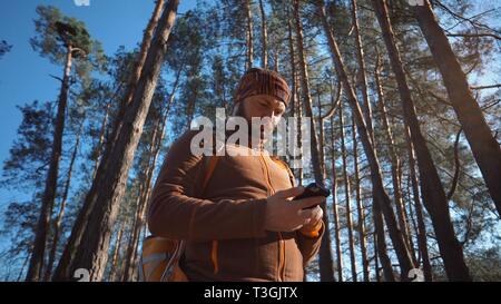 Thème du tourisme et de la technologie. Young caucasian man with beard et sac à dos. Tourisme de randonnée en forêt de pins utilise la technologie, main tenant téléphone mobile pour Banque D'Images