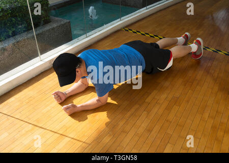 L'excès de l'homme faisant plank exercer dans une salle de gym avec plancher en bois par un pool - Horizontal Banque D'Images