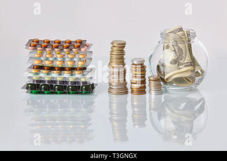 Pack de médecine pills avec trois paquets de pièces et le flacon en verre avec de l'argent en dollars sur une table en verre blanc avec reflet miroir Banque D'Images