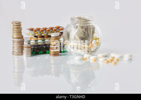 Pack de médecine pills avec trois paquets de pièces et le flacon en verre avec de l'argent en dollars sur une table en verre blanc avec reflet miroir Banque D'Images