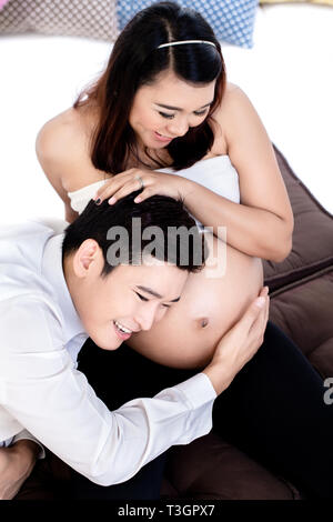 Smiling man listening to his pregnant wife's belly Banque D'Images