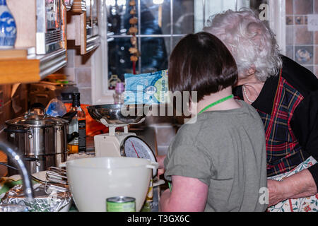 Jeune fille avec le syndrome de Down à la vie quotidienne d'apprentissage avec sa grand-mère dans la cuisine. Banque D'Images