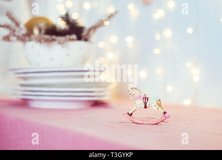 Composition avec arbre de Noël vintage porcelaine jouet figurine d'un cheval à bascule et des plats sur la table rose sur l'arrière-plan de Lumières floues. Fe Banque D'Images